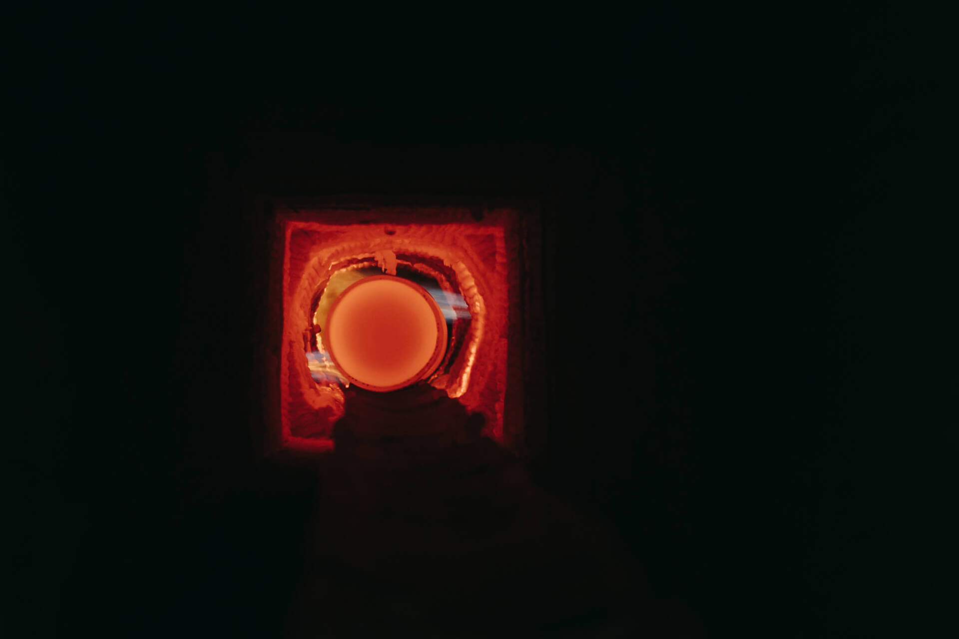 A glowing, orange orb is visible through a small opening in a dark, brick-lined furnace.