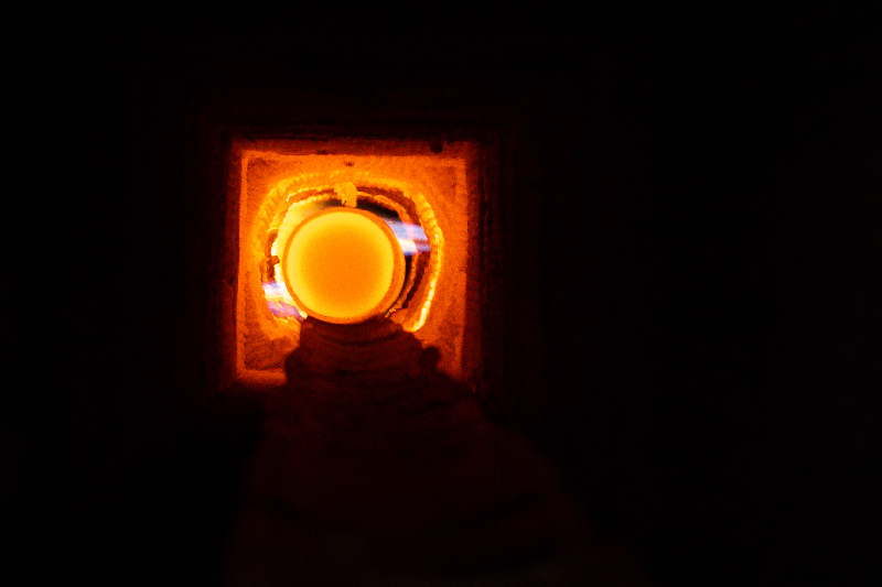 A glowing, orange orb is visible through a small opening in a dark, brick-lined furnace.